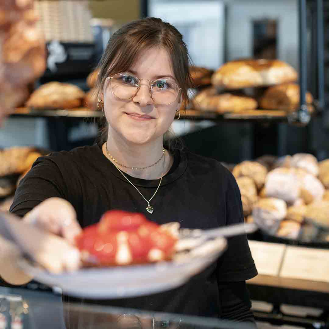 Smiling employee from Holms Bakery giving a cake to a customer.